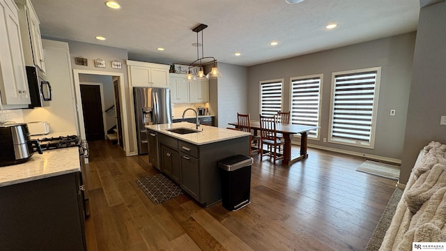 kitchen featuring hanging light fixtures, a kitchen island with sink, sink, white cabinetry, and stainless steel fridge with ice dispenser