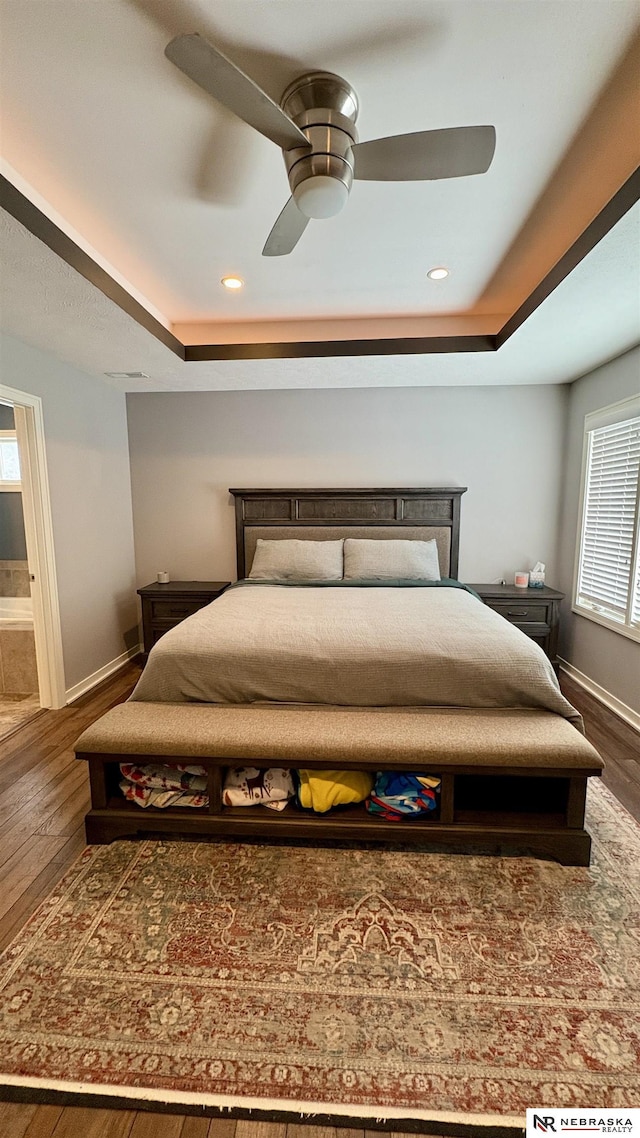 bedroom with a tray ceiling, dark wood-type flooring, and ceiling fan