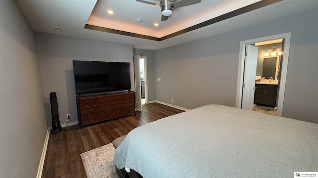 bedroom with a raised ceiling, ceiling fan, ensuite bathroom, and dark wood-type flooring