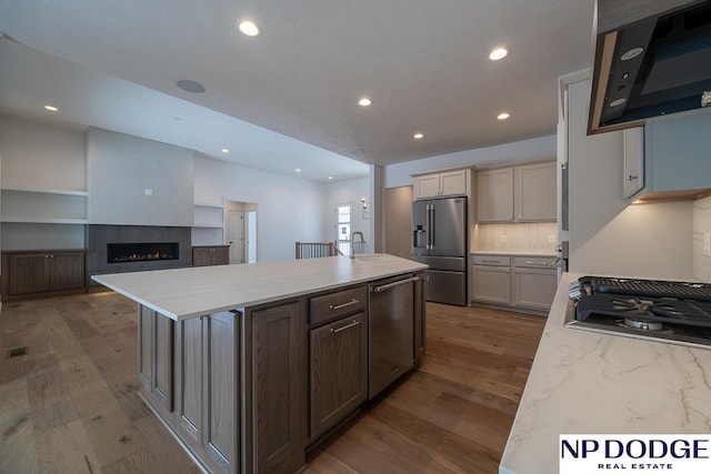 8909 Appaloosa Ln, Lincoln, NE 68520 - kitchen with wood finished floors, a sink, a kitchen island with sink, a lit fireplace, and appliances with stainless steel finishes