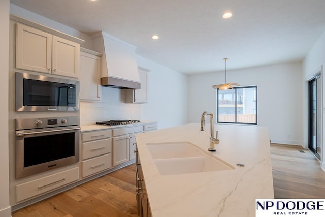8909 Appaloosa Ln, Lincoln, NE 68520 - kitchen with stainless steel appliances, light wood-style flooring, a sink, recessed lighting, and custom range hood