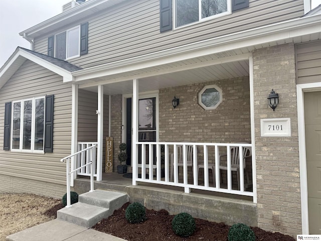 view of exterior entry with a porch and brick siding