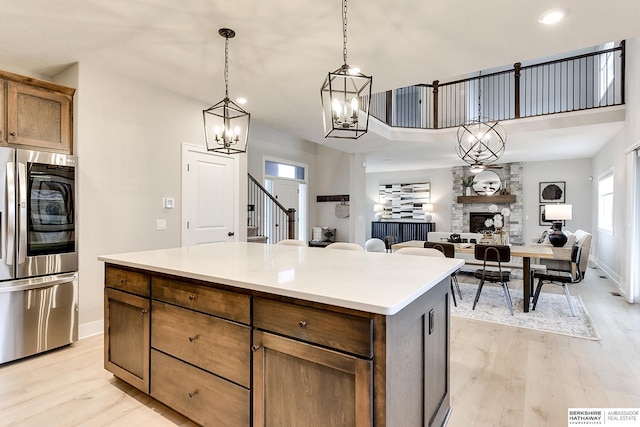 kitchen with a fireplace, a center island, stainless steel refrigerator with ice dispenser, light hardwood / wood-style floors, and pendant lighting