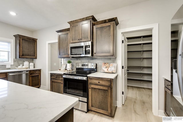 kitchen with backsplash, dark brown cabinets, stainless steel appliances, and light hardwood / wood-style floors