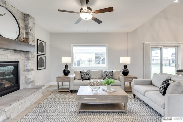 living room featuring ceiling fan and a stone fireplace