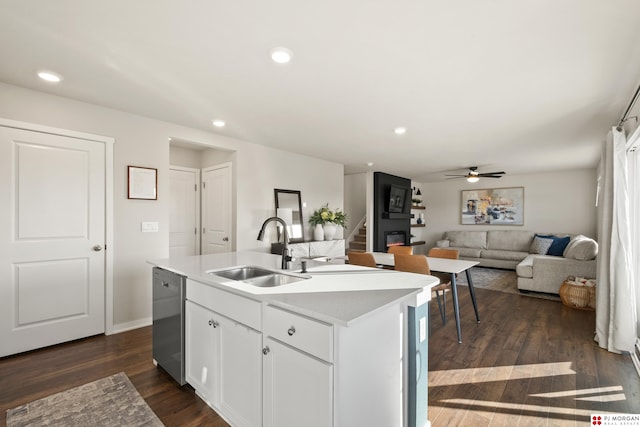 kitchen featuring an island with sink, sink, stainless steel dishwasher, dark wood-type flooring, and white cabinets