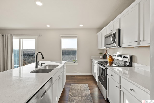 kitchen with appliances with stainless steel finishes, dark wood-type flooring, light stone countertops, white cabinets, and sink