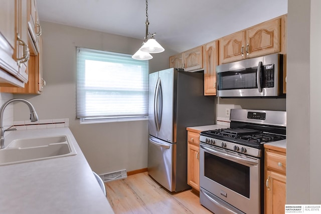 kitchen featuring light wood-type flooring, stainless steel appliances, decorative light fixtures, sink, and light brown cabinetry