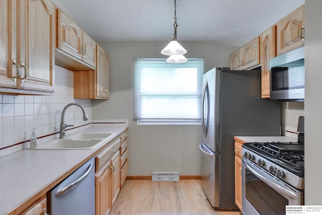 kitchen with hanging light fixtures, stainless steel appliances, light hardwood / wood-style flooring, sink, and backsplash