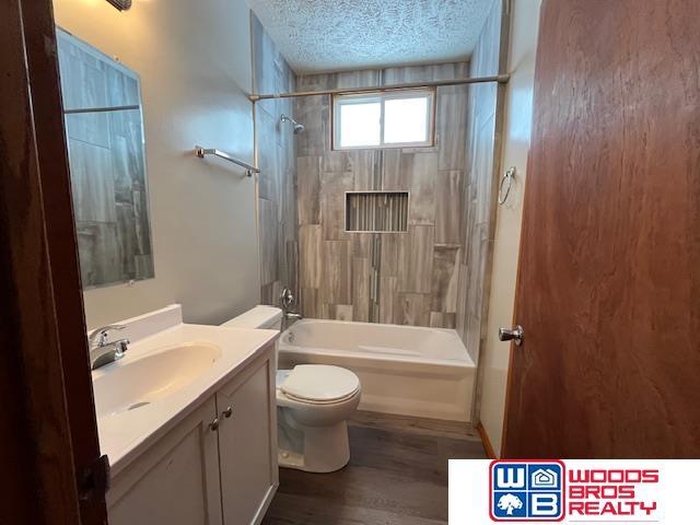 full bathroom featuring tiled shower / bath combo, toilet, wood-type flooring, a textured ceiling, and vanity