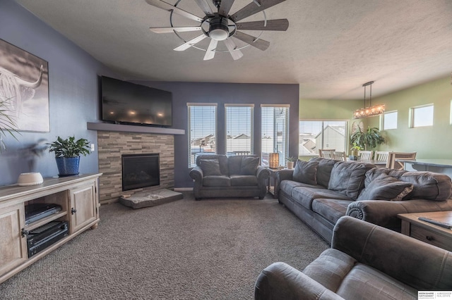 carpeted living room featuring a textured ceiling, a stone fireplace, and ceiling fan with notable chandelier