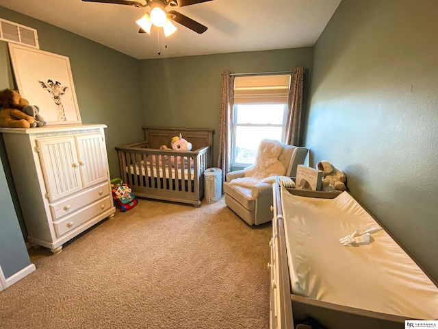 carpeted bedroom with a crib and ceiling fan