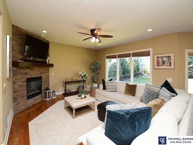 living room with hardwood / wood-style flooring, ceiling fan, a stone fireplace, and a textured ceiling