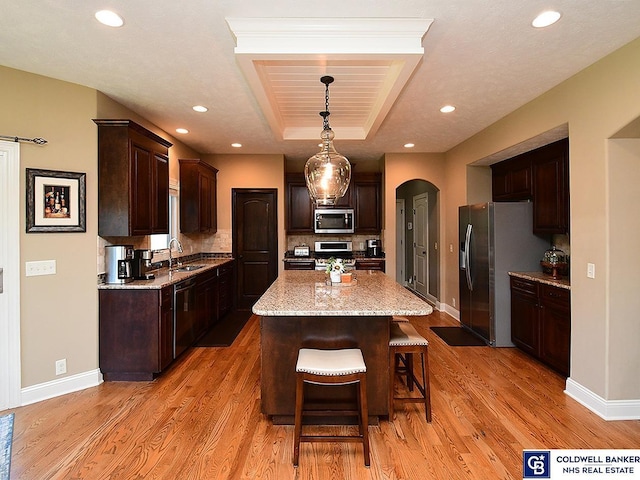 kitchen featuring stainless steel appliances, a center island, decorative light fixtures, dark brown cabinets, and a raised ceiling