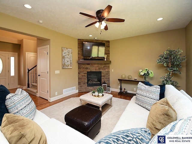 living room featuring light wood-type flooring, ceiling fan, a stone fireplace, and a textured ceiling