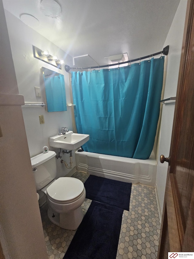 bathroom featuring a sink, shower / bath combo with shower curtain, and toilet