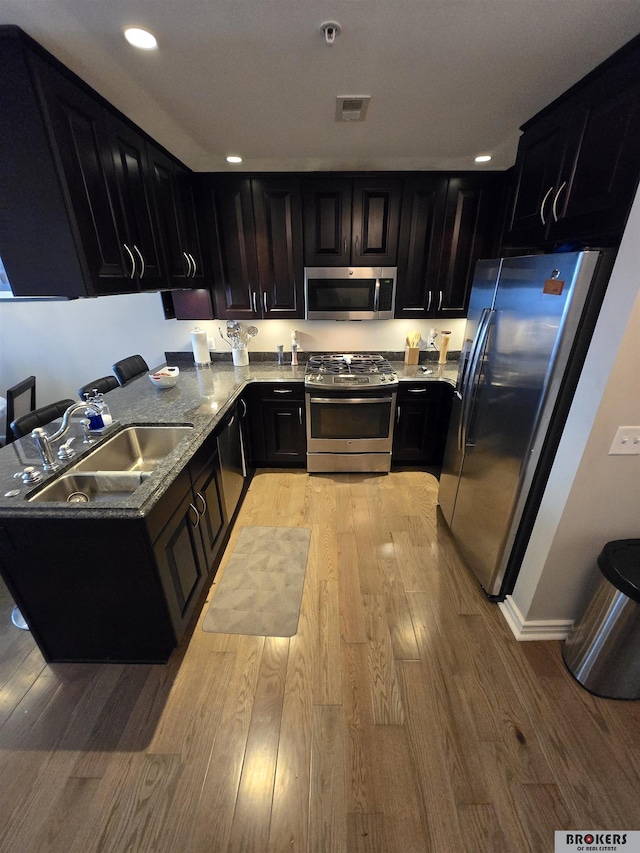 kitchen with light wood-type flooring, sink, light stone countertops, and stainless steel appliances