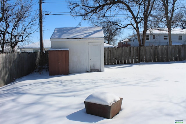 snowy yard featuring a storage shed, an outdoor structure, and a fenced backyard