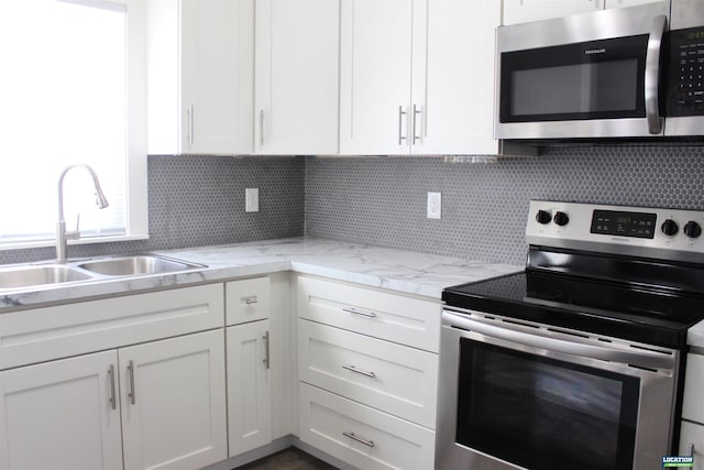 kitchen with appliances with stainless steel finishes, white cabinets, a sink, and decorative backsplash