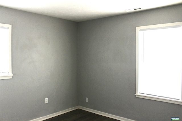 unfurnished room with visible vents, dark wood finished floors, and baseboards