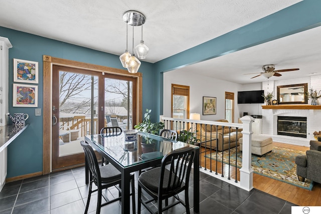 dining area featuring dark tile patterned floors, ceiling fan, a textured ceiling, and a fireplace