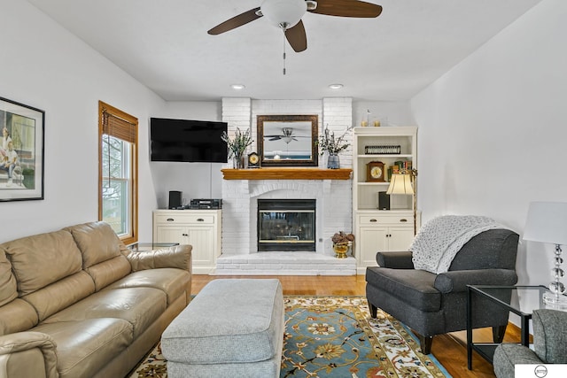 living room featuring a fireplace, light wood-type flooring, and ceiling fan