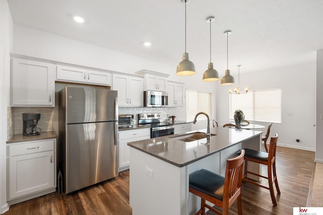 kitchen with a center island with sink, appliances with stainless steel finishes, dark wood-style flooring, a kitchen bar, and a sink