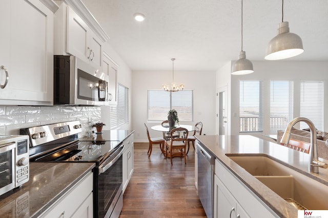 kitchen with tasteful backsplash, dark wood finished floors, dark stone counters, appliances with stainless steel finishes, and a sink