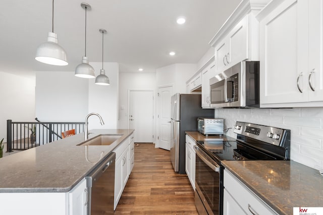 kitchen featuring a center island with sink, stainless steel appliances, tasteful backsplash, a sink, and wood finished floors