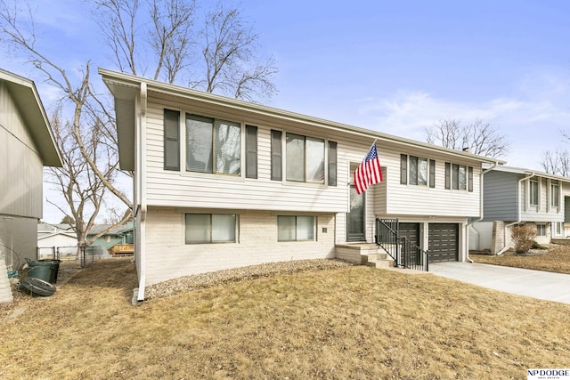 bi-level home featuring a front yard, a garage, brick siding, and concrete driveway