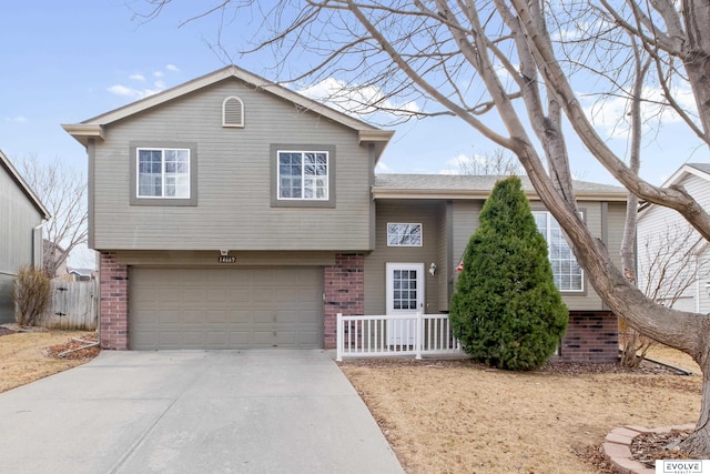 split level home featuring fence, brick siding, an attached garage, and concrete driveway