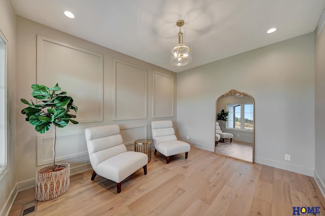 living area with light wood-type flooring, visible vents, baseboards, and a notable chandelier