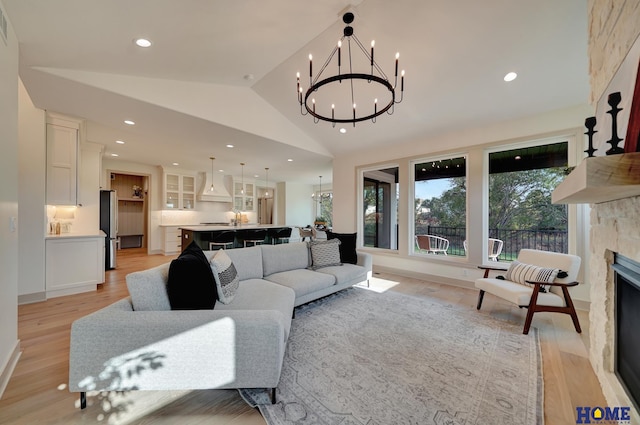 living room featuring a stone fireplace, a chandelier, recessed lighting, light wood finished floors, and vaulted ceiling