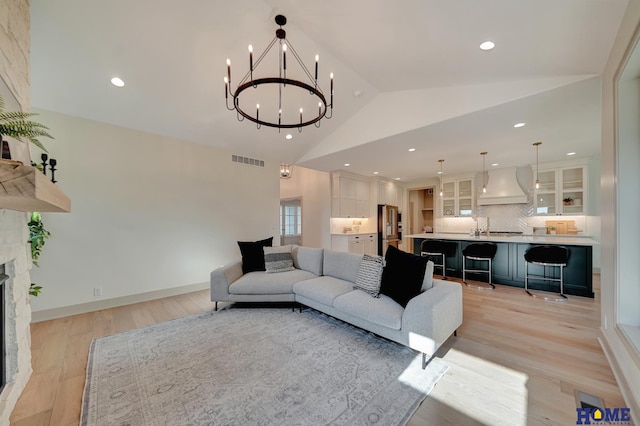 living room with a stone fireplace, visible vents, lofted ceiling, light wood-style floors, and a notable chandelier