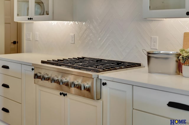 kitchen with stainless steel gas stovetop, light countertops, and glass insert cabinets