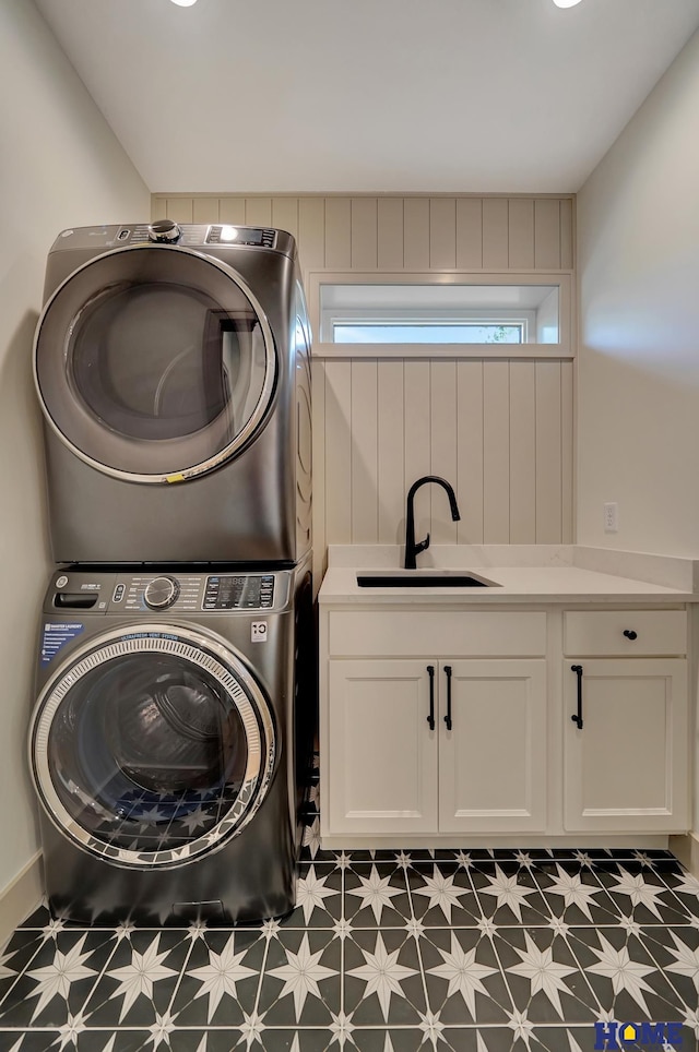 laundry room with a sink, stacked washer and clothes dryer, dark floors, and cabinet space