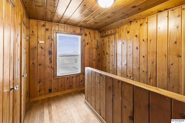 hallway featuring wood walls, baseboards, wooden ceiling, light wood-style floors, and a sauna