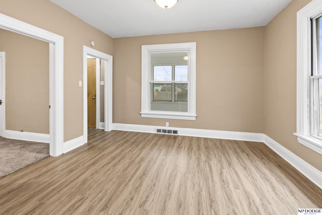 empty room featuring light wood finished floors, visible vents, and plenty of natural light