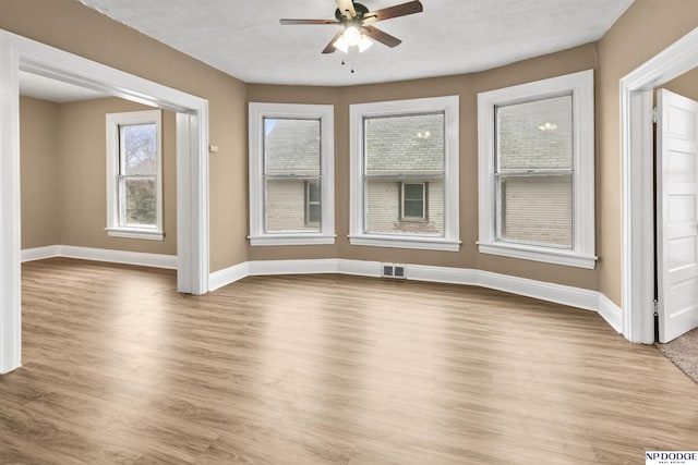 empty room featuring a ceiling fan, visible vents, baseboards, and light wood-type flooring