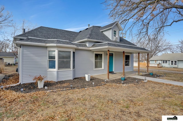 view of front of house with a shingled roof, a front yard, and a patio