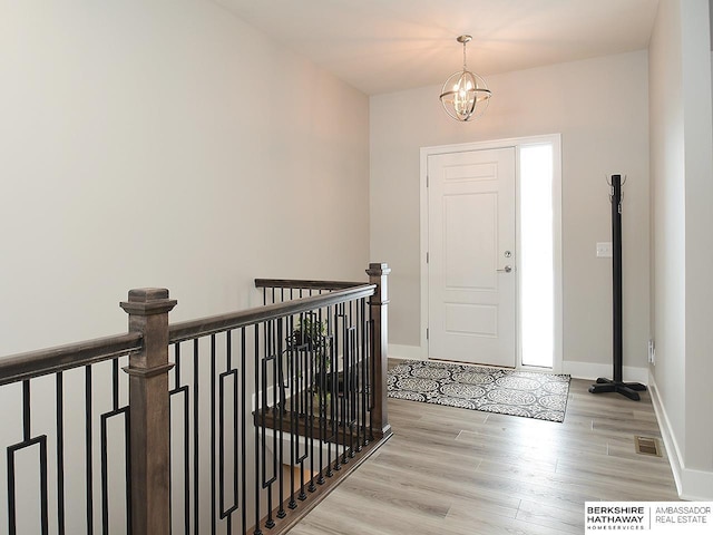 entryway featuring an inviting chandelier, light wood-type flooring, visible vents, and baseboards