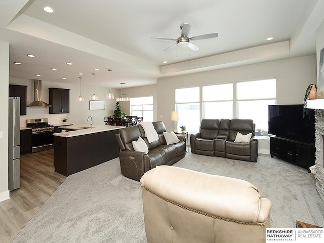 living room featuring light wood-style floors, a tray ceiling, a ceiling fan, and recessed lighting