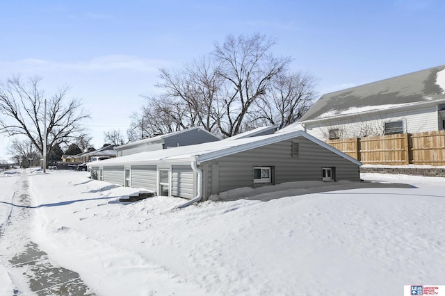 snow covered rear of property featuring a garage and fence