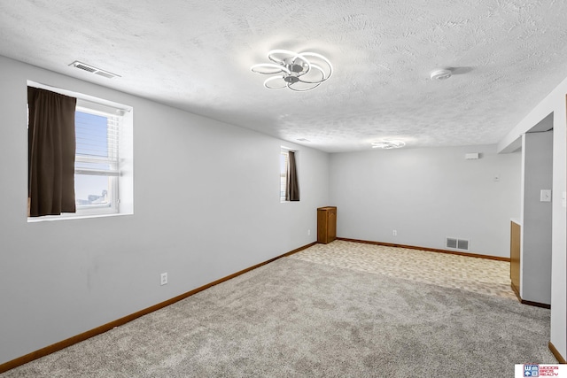 basement featuring baseboards, visible vents, a textured ceiling, and carpet flooring