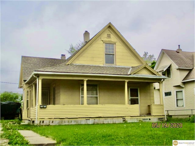 view of front of home featuring covered porch, a shingled roof, a chimney, and a front lawn