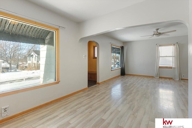 spare room featuring arched walkways, baseboards, a ceiling fan, and light wood-style floors