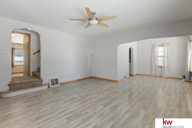 unfurnished living room featuring visible vents, arched walkways, light wood-style flooring, ceiling fan, and stairway