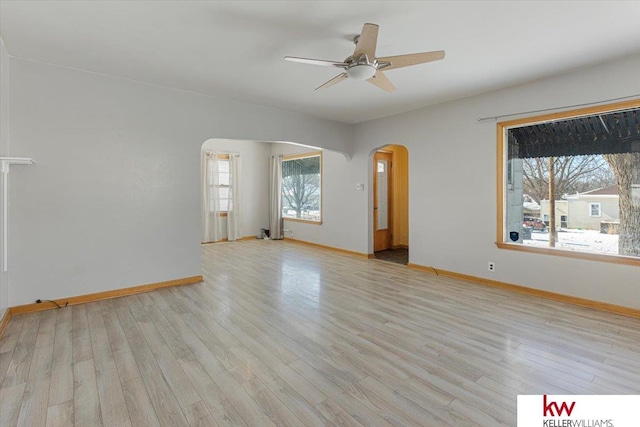 spare room with light wood-style floors, arched walkways, and baseboards