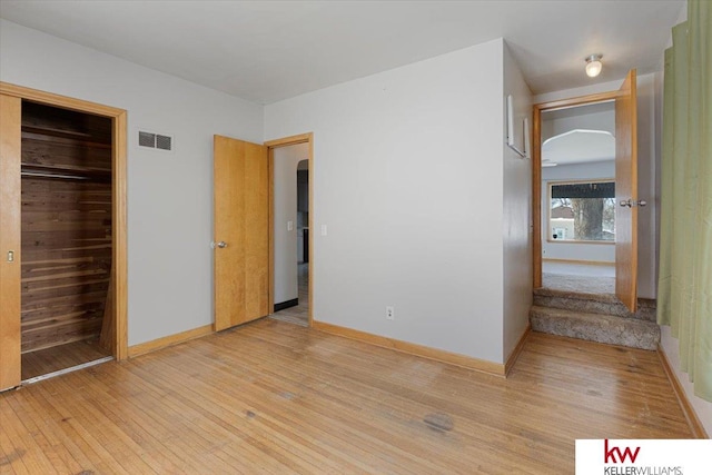 unfurnished bedroom with arched walkways, baseboards, visible vents, and light wood finished floors