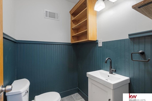 half bath with toilet, wainscoting, vanity, and visible vents